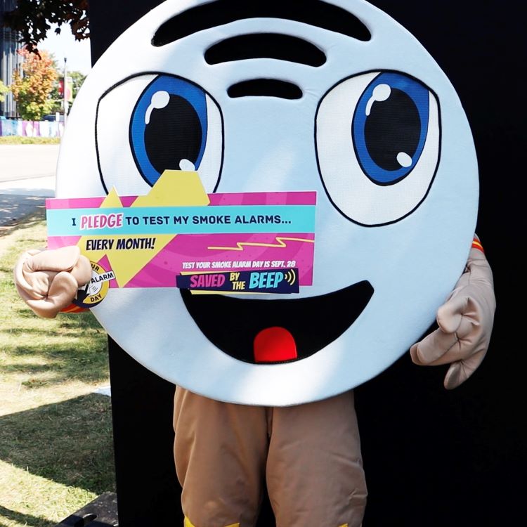 Picture of Beepa the Smoke Alarm mascot costume, holding a pledge sign made by Office of the Fire Marshal, promoting this year’s Saved By the Beep fire safety campaign.